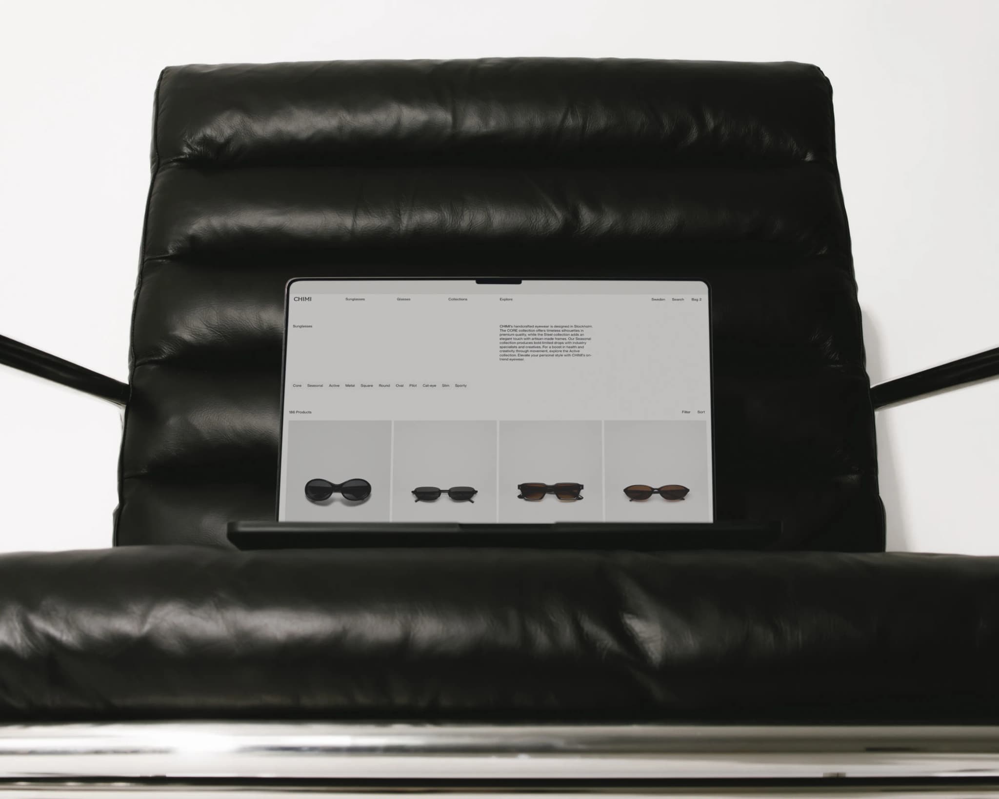 A laptop displaying Chimis sunglasses, positioned on a black leather chair with metal legs, is seen in a minimalistic setting.