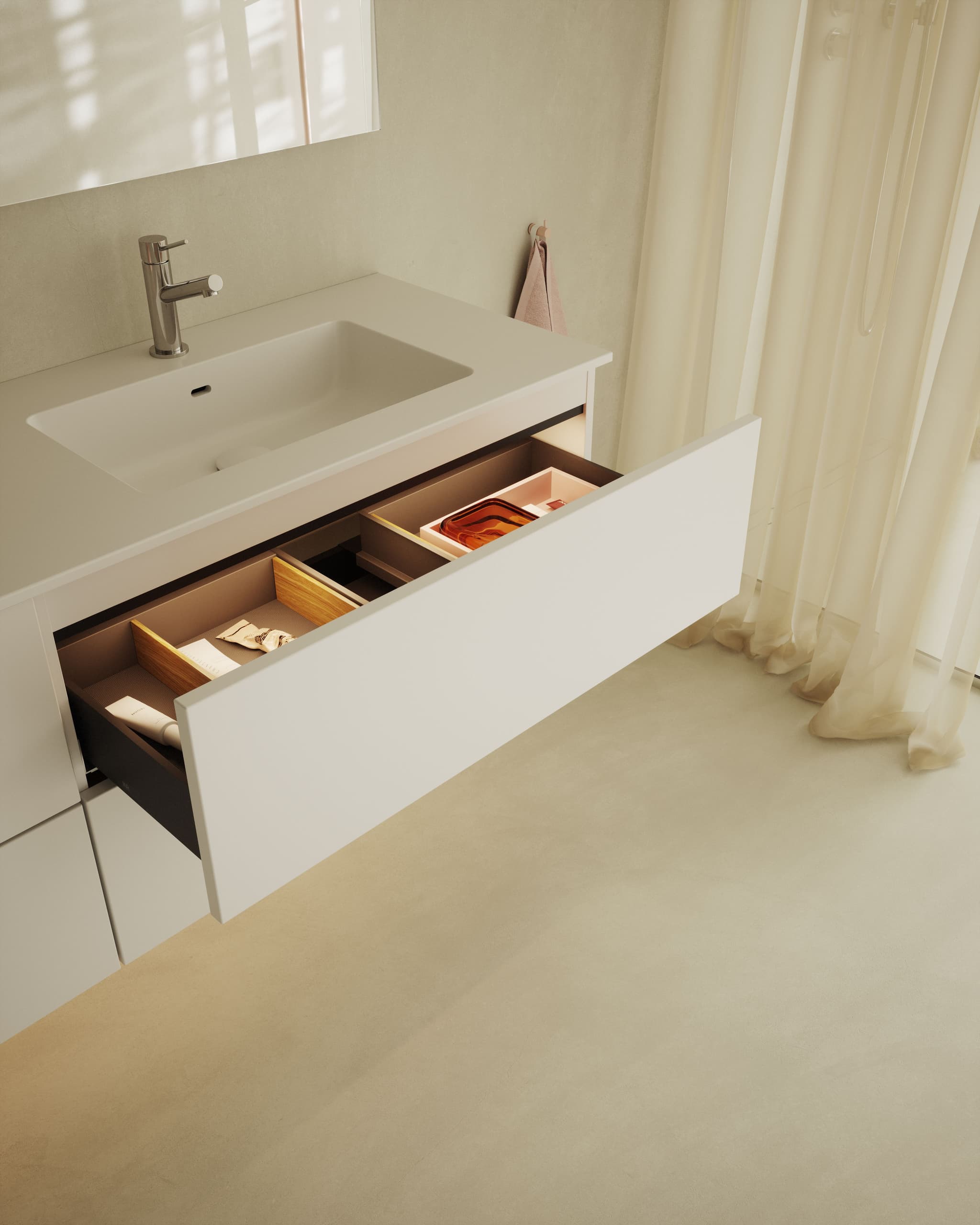 Open bathroom drawer under a white sink, organized with neatly arranged toiletries and wooden dividers, next to sheer curtains.